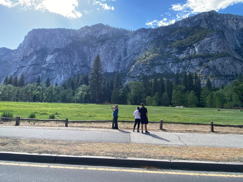 Visitors walking through Yosemite Valley with waterfall and cliffs in background